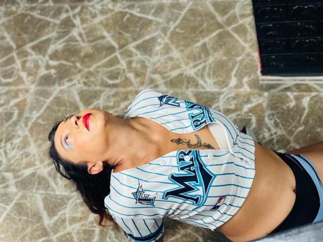 MatureFontana, allongée sur le dos, porte un maillot de hockey rayé bleu et blanc, qui dévoile sa poitrine et son ventre, avec du rouge à lèvres et un tatouage au-dessus de sa poitrine..