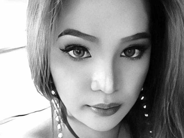 TrannyCumX hat ein attraktives Gesicht mit dicken, dunklen Augenbrauen, langen Wimpern und glänzlichen Lippen. Sie trägt Perlenohrringe und hat kurze, wellige Haare. Schwarz-weiß-Foto..