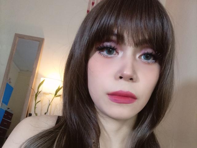 TSAnabelleSwift has long brown hair, pink eyeshadow, and pink lipstick, with blue eyes and a neutral expression, showing her face and upper shoulders. Her nose is small and cute.