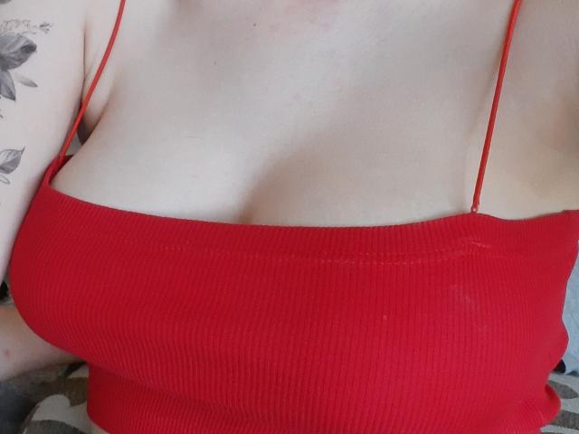 Destinis' red ribbed tank top, showing her boobs, with thin red straps, and a tattooed arm on the left. Her pale skin contrasts with the vibrant top.
