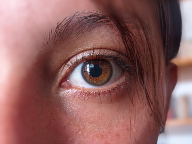 VictoriaOrtega's eye, brown with a small black pupil, slightly squinted, with a few brown eyebrows and a single brown eyelash visible. Her skin is light with some freckles.