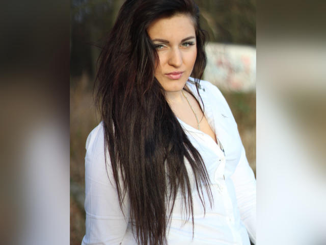EvelinCute with long, wet, dark brown hair, wearing a white button-up shirt, has blue eyes, and a slight smirk. Her tits are covered, but her ass is not visible.