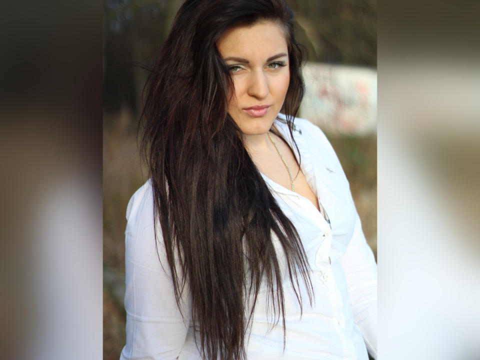 EvelinCute, con cabello largo, mojado y castaño oscuro, lleva una camisa blanca abotonada, tiene ojos azules y una ligera sonrisa. Sus pechos están cubiertos, pero su trasero no es visible..