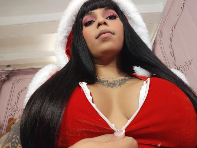 Chili's got her black hair down, big red lingerie with white trim, huge titties, and tattoos, looking down at the camera.