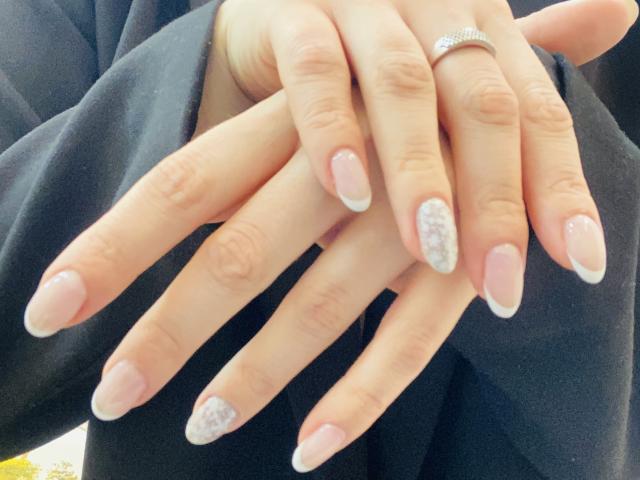 As mãos de KarKutie com esmalte de unhas rosa e prateado com glitter, dedos cruzados, usando uma luva preta e um anel de prata no dedo anelar direito..