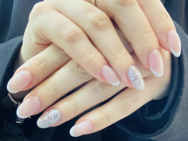 KarKutie's hands with pink, almond-shaped nails and one nail covered in white glitter, fingers gently crossed, pale skin, black sleeve, soft light.