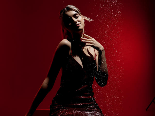 Jasmine, vêtue d'une robe noire scintillante, les mains sur le cou, éclairage rouge, gouttes d'eau, yeux fermés, maquillage discret, sexy, confiante, pose séduisante, silhouette mince, petites seins..