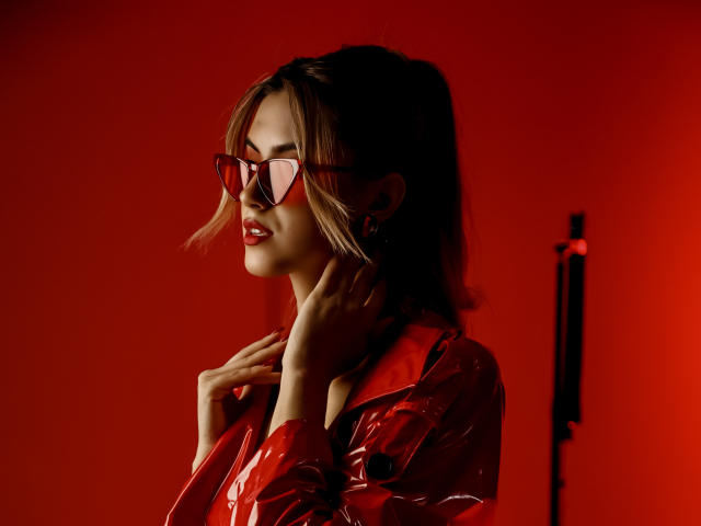 JasmineDay com óculos de armação vermelha, jaqueta vermelha brilhante, mãos perto do rosto, olhando para o lado, batom vermelho, corpo de tamanho médio, cabelo loiro, fundo vermelho, iluminação suave, sexy, confiante, elegante..