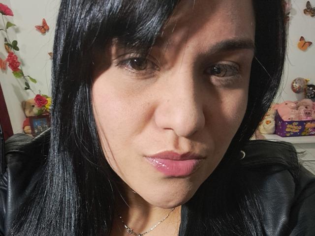 Viviana Thompson tiene el cabello negro y brillante, ojos marrones y labios rosados y lustrosos. Lleva una chaqueta de cuero negra, y su rostro está ligeramente fruncido. Es una mujer latina..