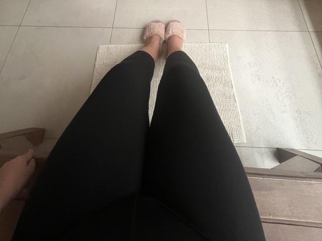 Barbarica's zwarte benen, bedekt met een broek, met roze, veterschoenen, staan op een witte mat, waarbij haar blote voeten te zien zijn, op een betegelde vloer. Haar vagina is niet zichtbaar..