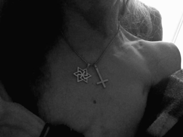 OscuroInverno's blote borst, met een Davidster-ketting en een kruis-ketting, met een kleine moel onder de nek, op een zwart-wit foto..