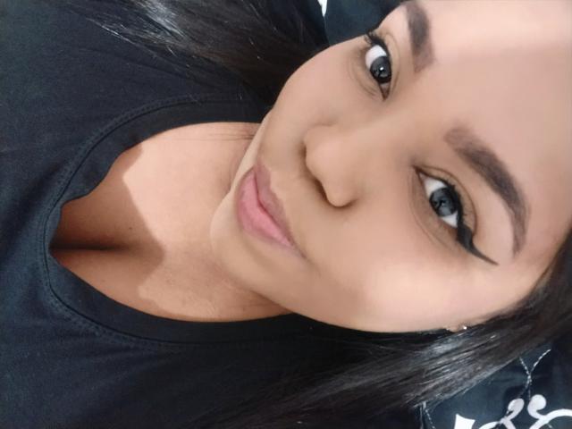 SarahSmity ha la pelle olivastra, l'eyeliner nero e un sorriso carino. Indossa una maglietta nera e i suoi lunghi capelli neri sono parzialmente visibili. I suoi occhi sono rivolti verso la fotocamera..