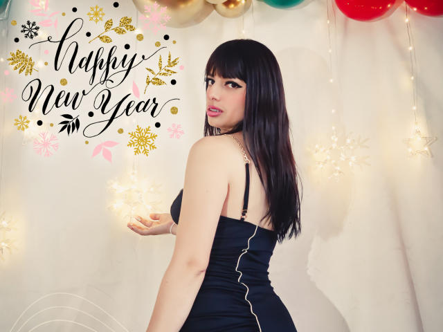 LeticiaFlorenz with long black hair, wearing a black dress, turning to show her back and ass, looking over her shoulder, in front of festive lights and balloons.