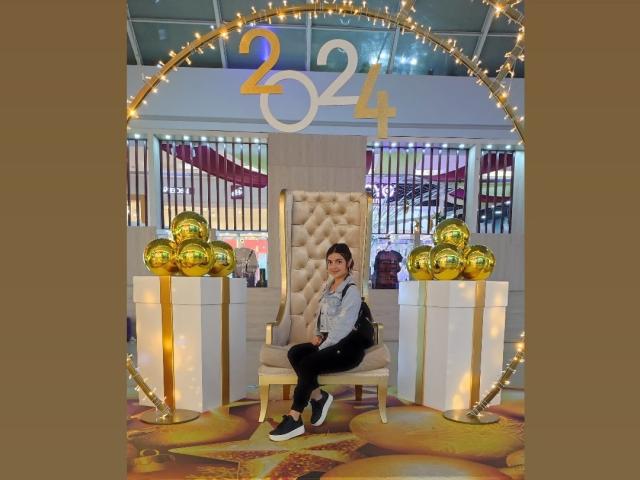 HeidyMillerr sits in a beige tufted chair, wearing a gray shirt, black pants, and white sneakers, with gold balloons and numbers 24 above her.