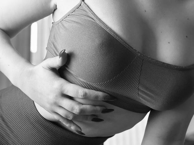 SugarrX's hand with dark nails grips her large, ribbed sports bra, covering her tits. She's wearing high-waisted, ribbed pants, in a black-and-white shot.