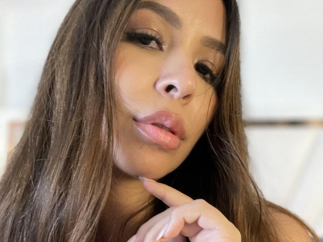 MeganWisse's face with full lips, brown eyes, and long brown hair, slightly parted pink lips, touching her chin with her finger, soft light, subtle makeup.