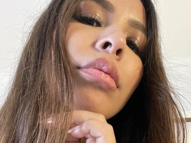 MeganWisse's pouty lips are slightly pursed, her glossy brown eyes are half-closed, and her long brown hair falls over her face. Her hand rests near her chin.