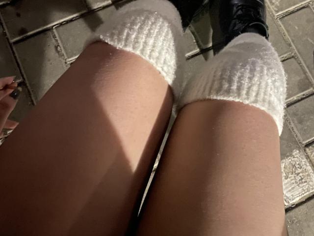 Los calcetines blancos de punto de Rubbi cubren sus piernas, con unas botas negras en la parte superior. Se puede ver su piel desnuda y una sombra, y lleva un anillo en la mano derecha..