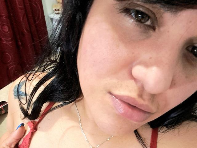 VivianaThompson has medium brown skin, black wavy hair, and is looking at the camera with slightly parted pink lips. She's wearing a red top, showing her small tits.