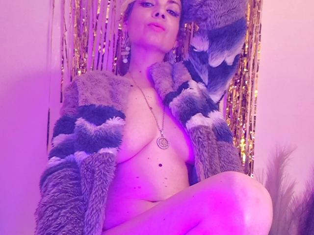 SassyMarry, naked, with large boobs, wearing a fuzzy striped cardigan, necklace, and purple light, sitting, looking at camera, smiling, hands in cardigan, purple glow, curly hair.