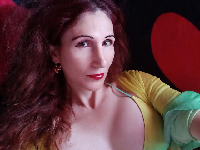 LovaLove has curly red hair, red lipstick, green-yellow dress, and is showing her tits with a cute smile. She's wearing star-shaped earrings and has a fair skin tone.
