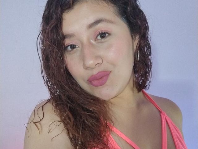 VeronicaHot69 con capelli castano ricci e bagnati, rossetto rosa, piercing al naso e top rosa con spalline sottili, che guarda la fotocamera con le labbra rosa leggermente dischiuse. Pelle chiara, trucco leggero, piccoli orecchini a cerchio..