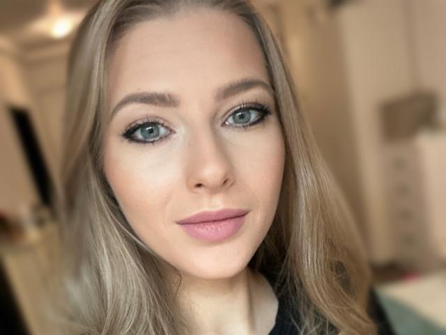 TheoRoss has green eyes, light makeup, and blonde hair with a subtle smile. She's wearing a black top, showing a pretty face with a cute ass.