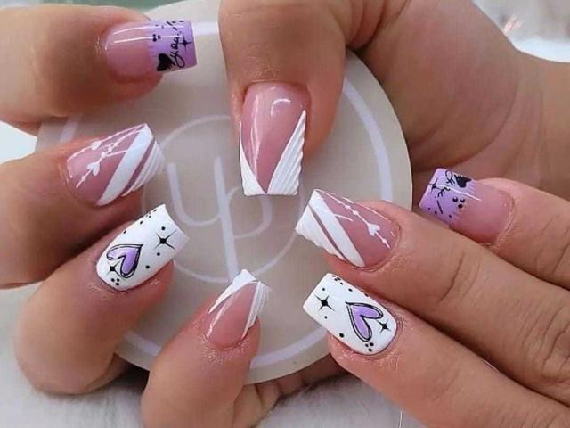 MalakCote's nails are painted with pink, white, and purple designs featuring arrows, hearts, and dots. Her nails are long with a French tip style, looking sexy.