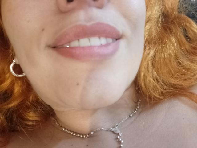 I capelli rossi di Joanallen, i suoi denti bianchi e il piercing all'argenteo labbro sono visibili. Indossa una collana d'argento con un ciondolo a forma di cuore e un orecchino a forma di mezzaluna..