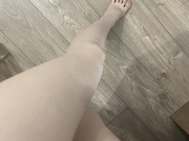 La gamba pallida, liscia e nuda di RozalinaPleasure, con una leggera ombra su un pavimento di legno, mostra il suo piede con le unghie delle dita dei piedi rosa. La sua coscia è parzialmente visibile..