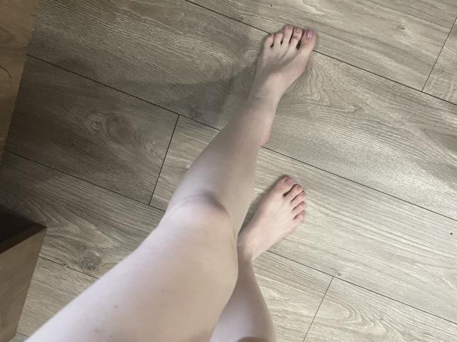 Las piernas pálidas de RozalinaPleasure estaban cruzadas a la altura de los tobillos, con los pies sobre un suelo de madera, y las uñas de los dedos de los pies pintadas de rosa. Sus dedos apuntaban hacia arriba, mostrando su piel lisa y desnuda..