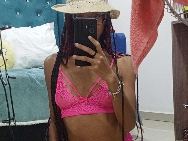 CanelaHott69 usando um sutiã de renda rosa, seios pequenos, vestindo um chapéu de palha, segurando um celular, selfie no espelho, tranças longas, pele bronzeada, pulseira no pulso direito, em pé em um quarto..