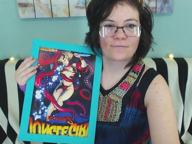 EverlyRays, a nerdy-looking chick with glasses, short black hair, and a colorful dress, holding a psychedelic "Mystereca" poster featuring a sexy, tentacled woman. Boobs not visible.