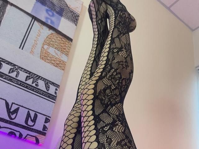 Tsukerberg in black lace fishnet dress, highlighting her tits and ass, with a tight, curvy figure, standing in profile, showcasing her sexy, seductive, and alluring appearance.