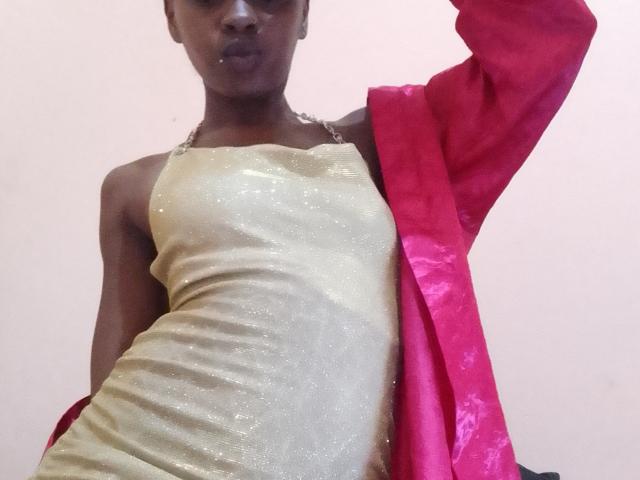 Eine LunaHottie mit dunkler Haut, die ein schimmerndes goldfarbenes Kleid und eine rote Jacke trägt, mit erhobenen Armen, die ihren kleinen, festen Hintern und ihre vollen Lippen zeigen, in einer lässigen Pose..