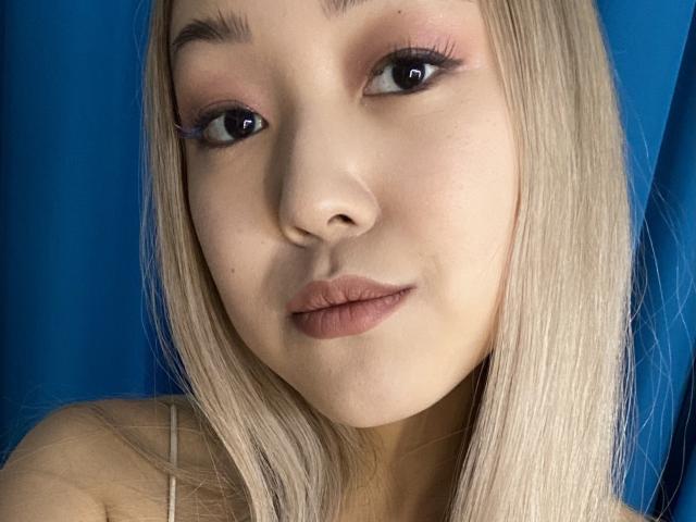 RenyLime has blonde hair, pink eyeshadow, and brown lipstick. She's making a pouty face with her lips slightly pressed together. Her blue eyes are looking at the camera.