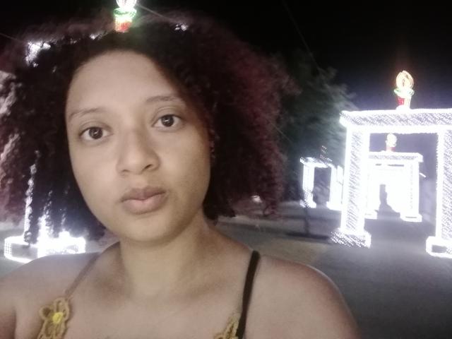 VioletaSwitch heeft een medium bruine huid, krullend donkerrood haar en draagt een zwart en geel topje. Ze maakt een fronsende gezicht in een nachtelijke selfie..