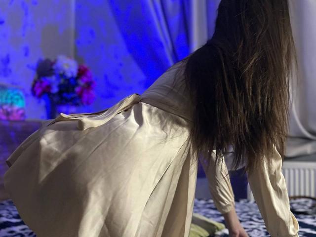 CheriLady is on all fours, wearing a silky beige dress, with her long brown hair flowing, showing her back and butt. Background is blurred.
