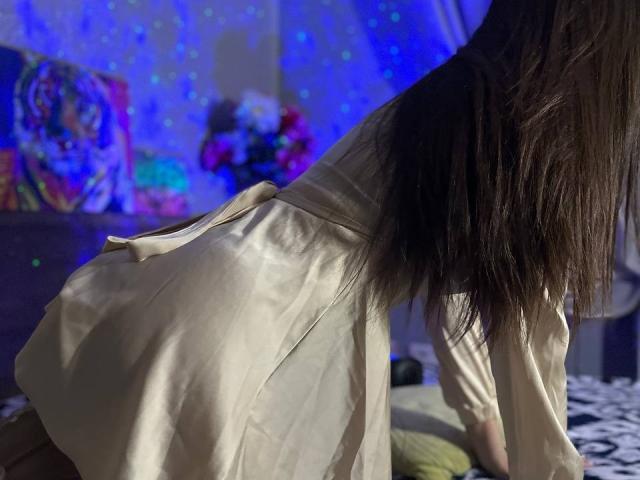 CheriLadys Hintern sind sichtbar, sie trägt ein seidiges, weißes Kleid, und ihr langes, braunes Haar fällt ihr herab. Ihr Rücken ist zur Kamera gerichtet, wodurch der elegante, fließende Stoff ihres Kleides hervorgehoben wird..