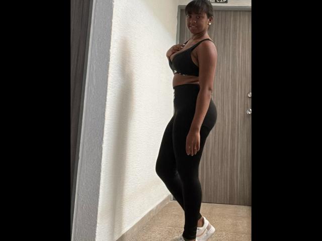 TiffanySammy standing in a room, wearing a black sports bra and high-waisted black leggings, with white sneakers, showing her ass and small tits, looking at the camera.