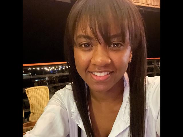 TiffanySammy has dark brown skin, long straight black hair with bangs, and a cute smile. She's wearing a white shirt, with visible small earrings. She's looking at the camera.