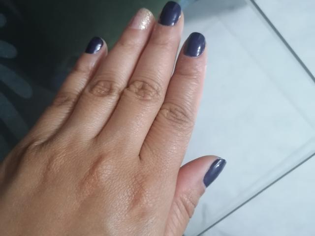 VioletaSwitch's hand with shiny, dark purple nails and a slightly glittery pinkie nail, placed flat against a glass surface. Her skin is light brown with visible wrinkles.
