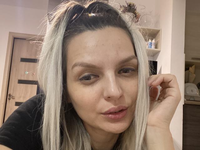 DouceAmelia with blonde hair, light skin, and brown eyes, pouty lips, and a small cut on her forehead, wearing a black top, looking at the camera.