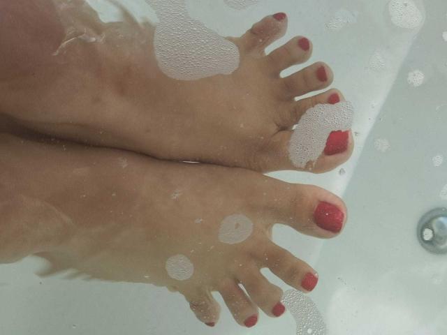 Los pies de PerfectLyly, con las uñas de los dedos de los pies pintadas de rojo, en una bañera blanca y jabonosa. Las burbujas cubren los dedos de los pies y la parte inferior de sus pies. Su piel es clara..