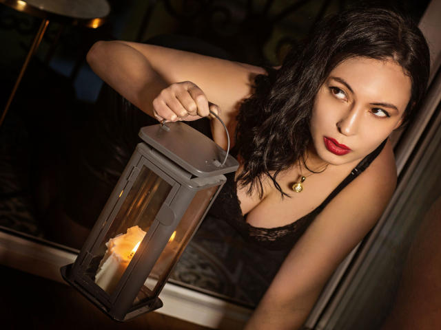 HotLioness with black wavy hair, red lipstick, and black lace dress, holding a lantern with a candle, looking sideways, sexy, curvy, medium tits, soft lighting, nighttime.