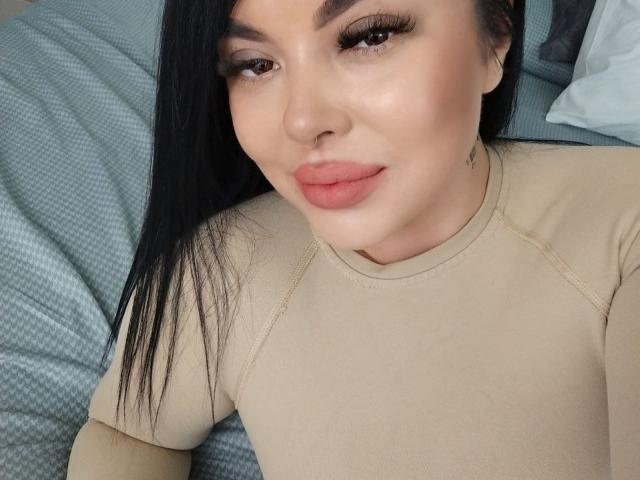 DarkElf tiene una cara linda con cabello negro largo, ojos marrones y labios rosados gruesos. Lleva una blusa color beige y está acostada sobre un cojín azul con estampado..