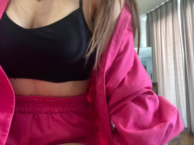 CheriLady trägt einen pinken Bademantel, einen schwarzen Sport-BH und pinke Shorts und zeigt dabei ihren nackten Bauch und ihre kleinen Brüste. Ihr braunes Haar fällt über ihre Schulter..