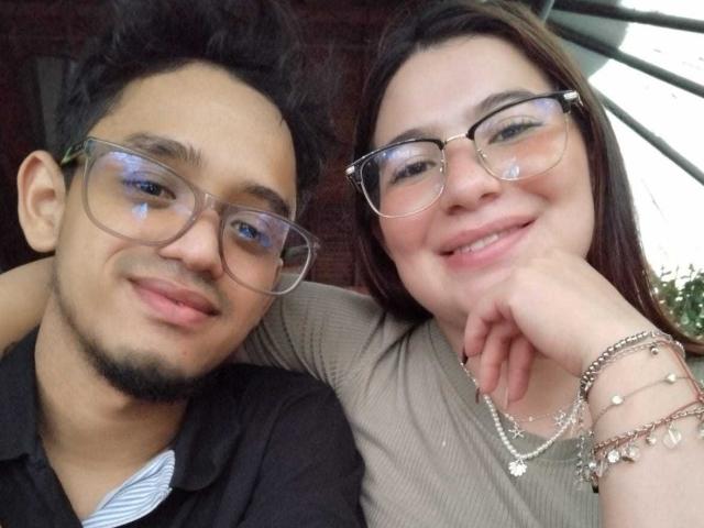 KayDwayne with glasses, short black hair, and a goatee, and KayDwayne with glasses, brown hair, and a smile, standing close, both wearing casual clothes, and bracelets.