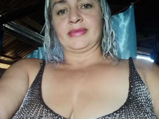 SalomeAriza has blue-tinted, wet-looking hair, pink lipstick, and a chubby face with medium tits in a black, mesh-patterned top. She's smiling slightly, looking at the camera.