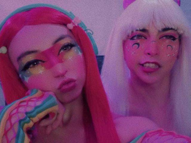 TheLesbianGame com cabelo rosa, maquiagem colorida e mangas com arco-íris, ao lado de TheLesbianGame com cabelo branco, maquiagem rosa e orelhas de gato, ambas com expressões emburradas..
